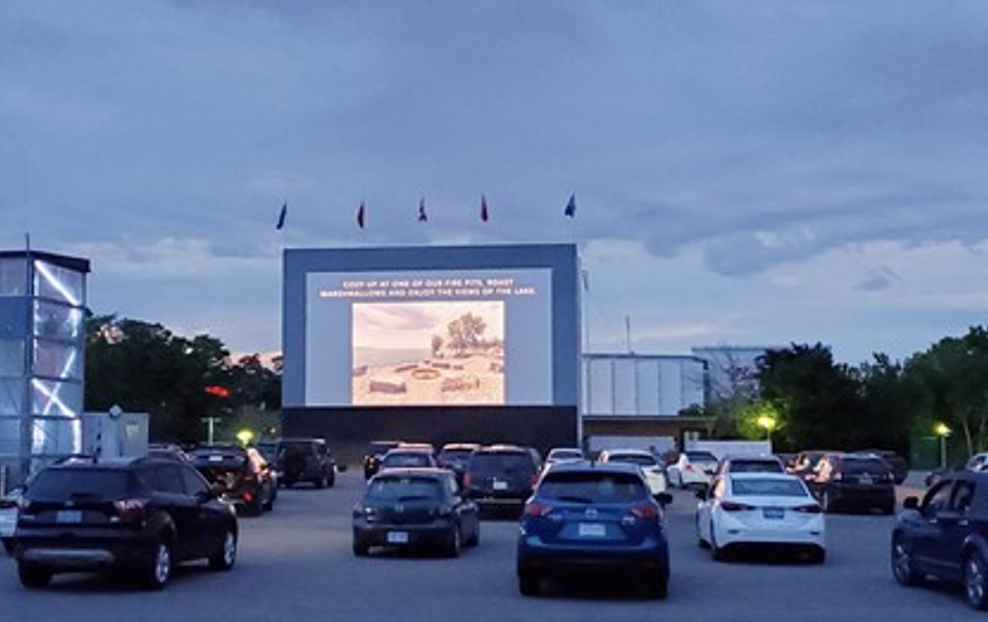 Image de voitures stationnées face à un grand écran projetant un film.  