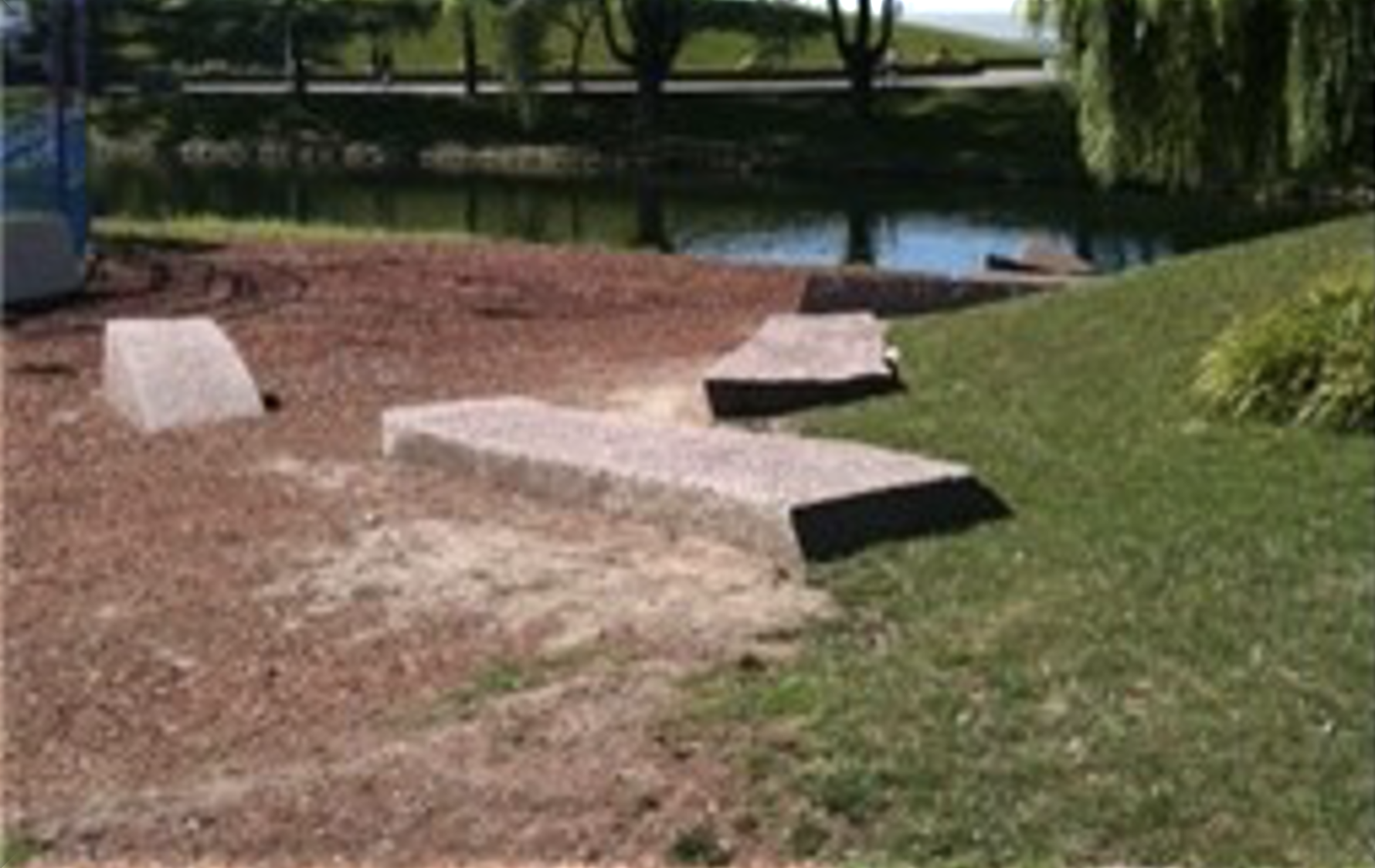 Image of three slabs of stones varying in size on a grassy area next to an inlet of water 