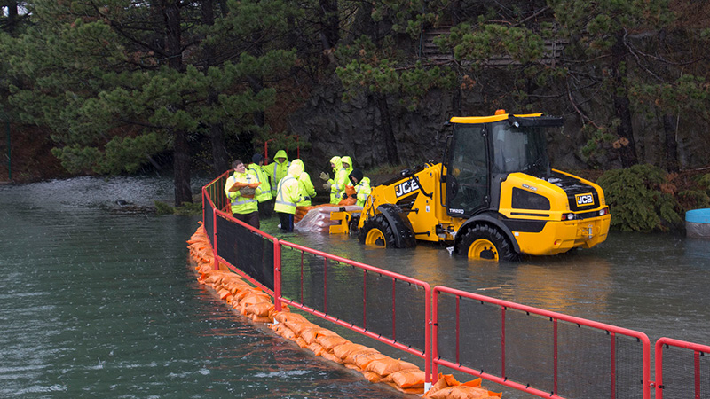 A group of people standing together wearing safety gear in a gated off area that has been flooded. They are next to large construction equipment.