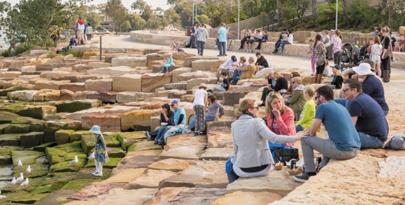 Image d’un groupe de personnes assises sur des paliers de gros rochers au bord de l’eau.