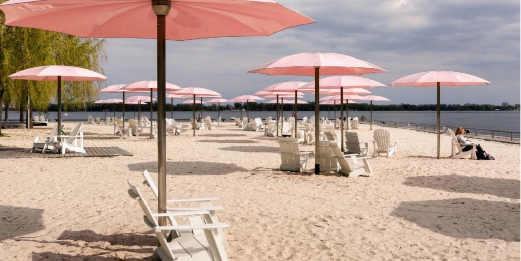 Photo d’une plage de sable avec des chaises en bois sous des parasols roses.