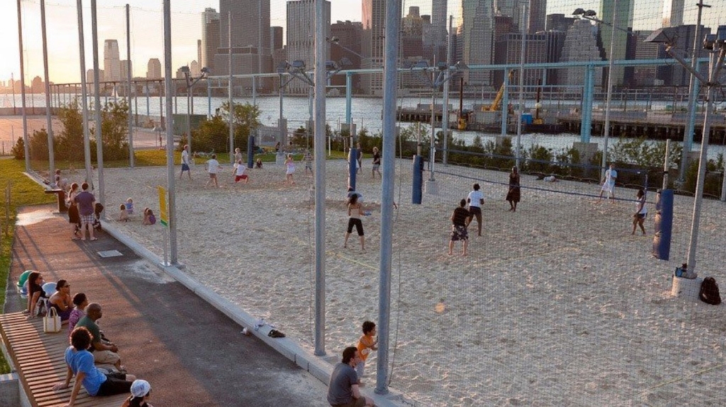 Picture of people playing volleyball on sand courts and city buildings in the background