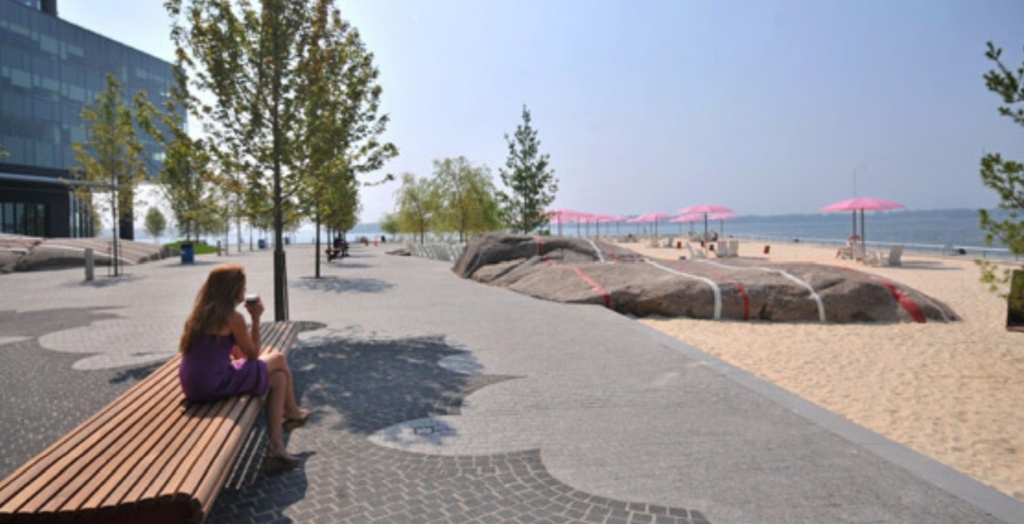 A person sitting on a bench on a paved pathway along a sandy beach