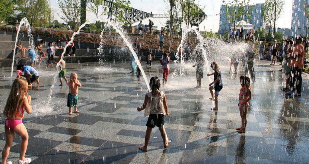 Photo d’enfants jouant dans une fontaine d’eau sur une surface pavée.
