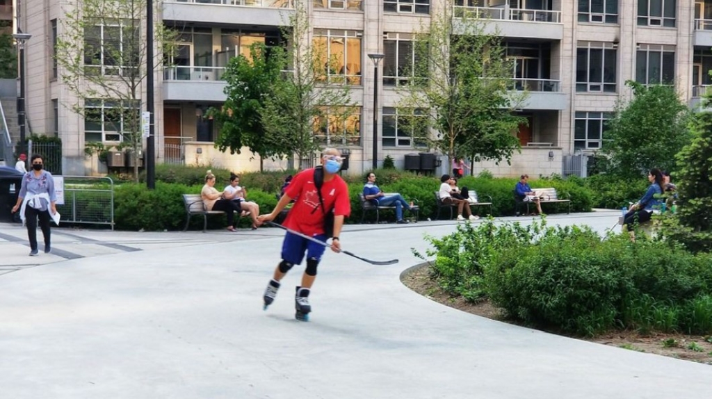 A picture of a person rollerblading with a hockey stick in their hand and people sitting on benches behind