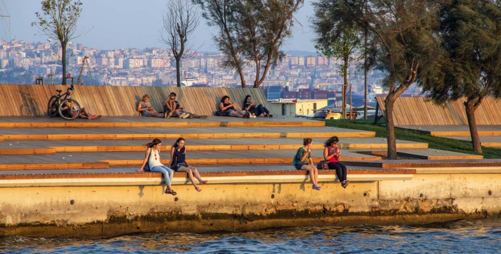 People sitting along a water edge with five terraced levels leading down to the water’s edge.