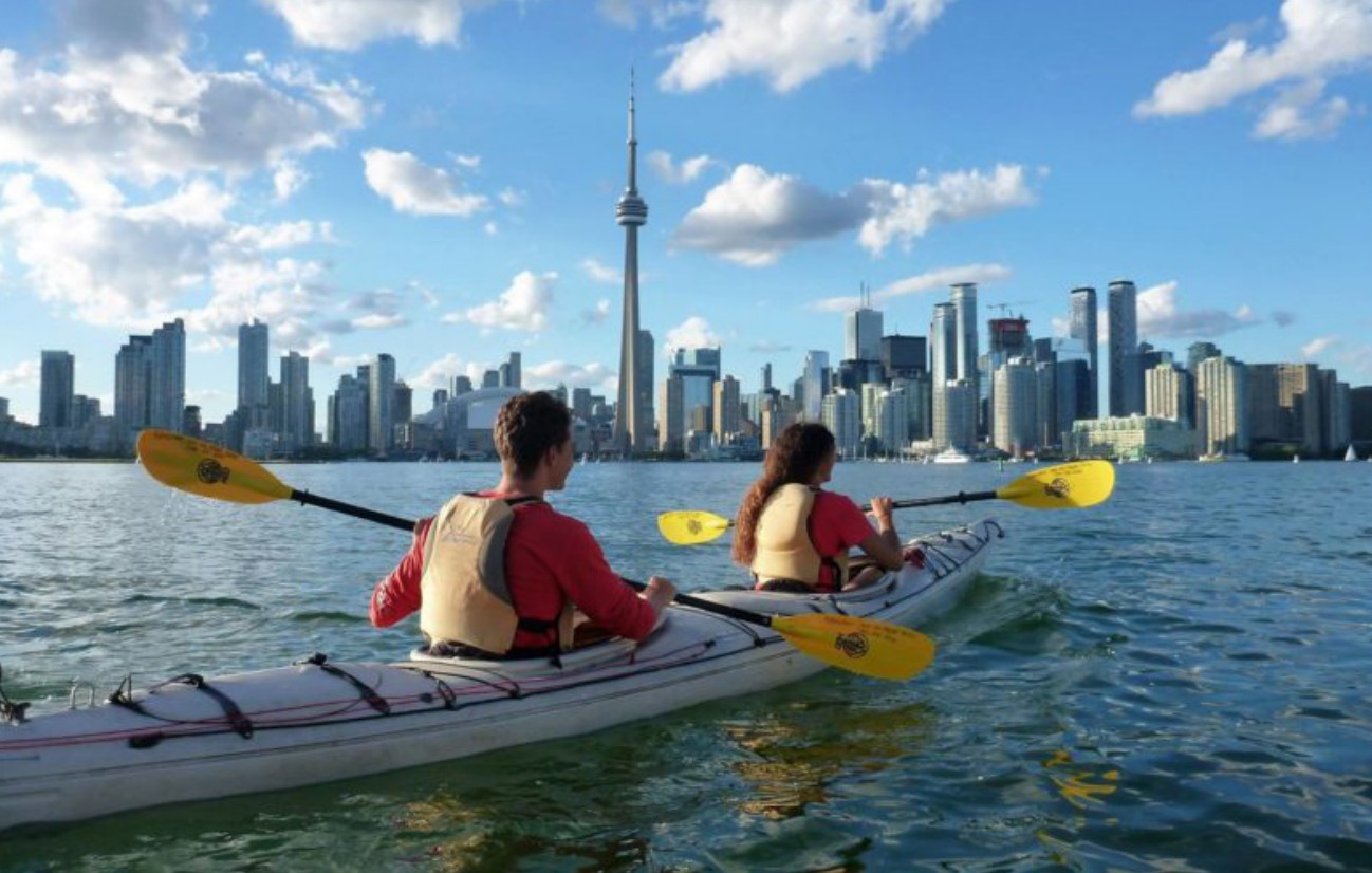 Two people kayaking in a two-person kayak with the Toronto city skyline in the background