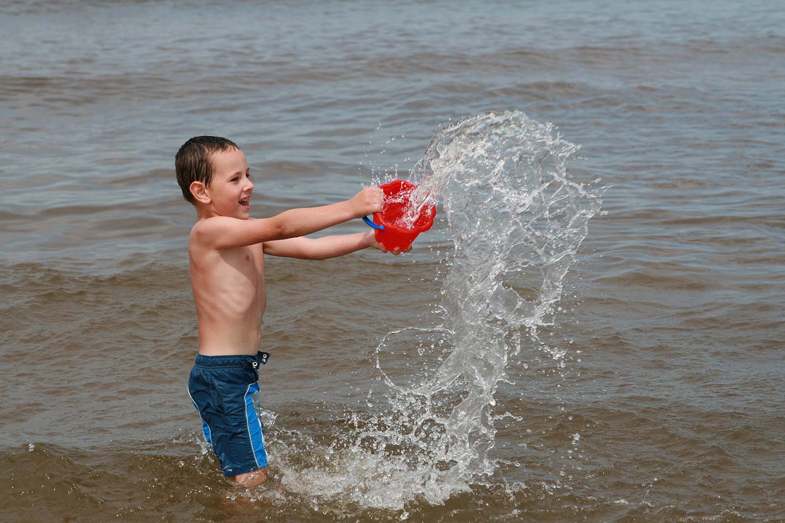 Enfant jouant avec un seau dans l’eau. 