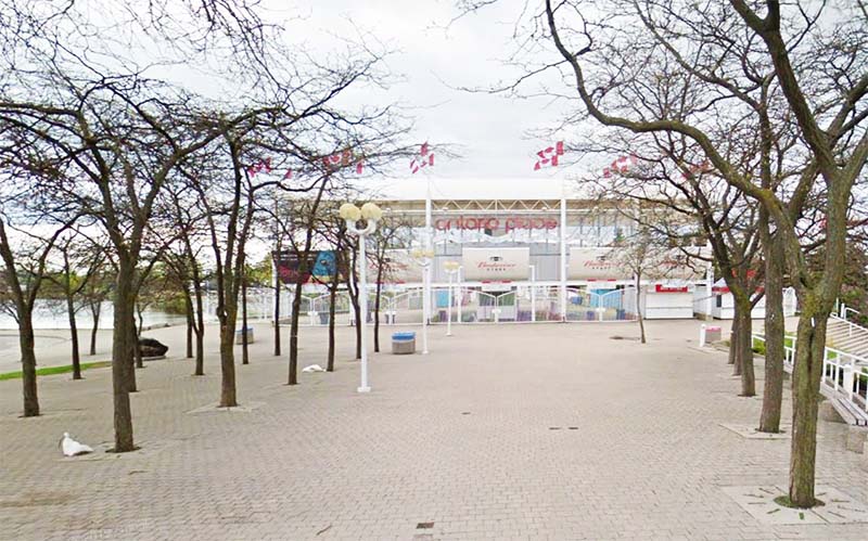 A picture of a paved walkway lined with trees, leading to a structure that has Ontario Place and Budweiser Stage signs on it