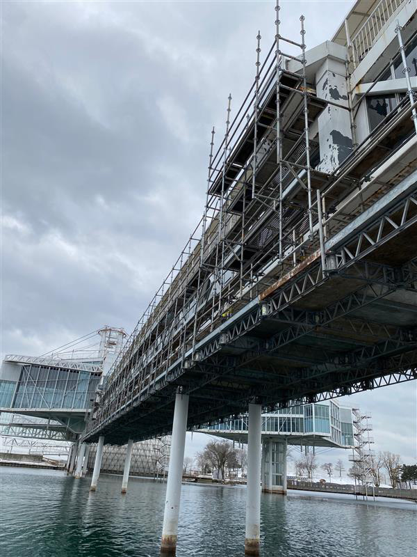 Scaffolding along a bridge raised over the water leading to the Pods at Ontario Place. 